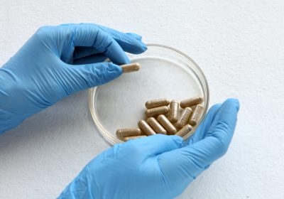 chemist at blue glowes at laboratory. testing with glass plate, organic pills at laboratory glass for medical testings. herbal capsules from ginger on white background.